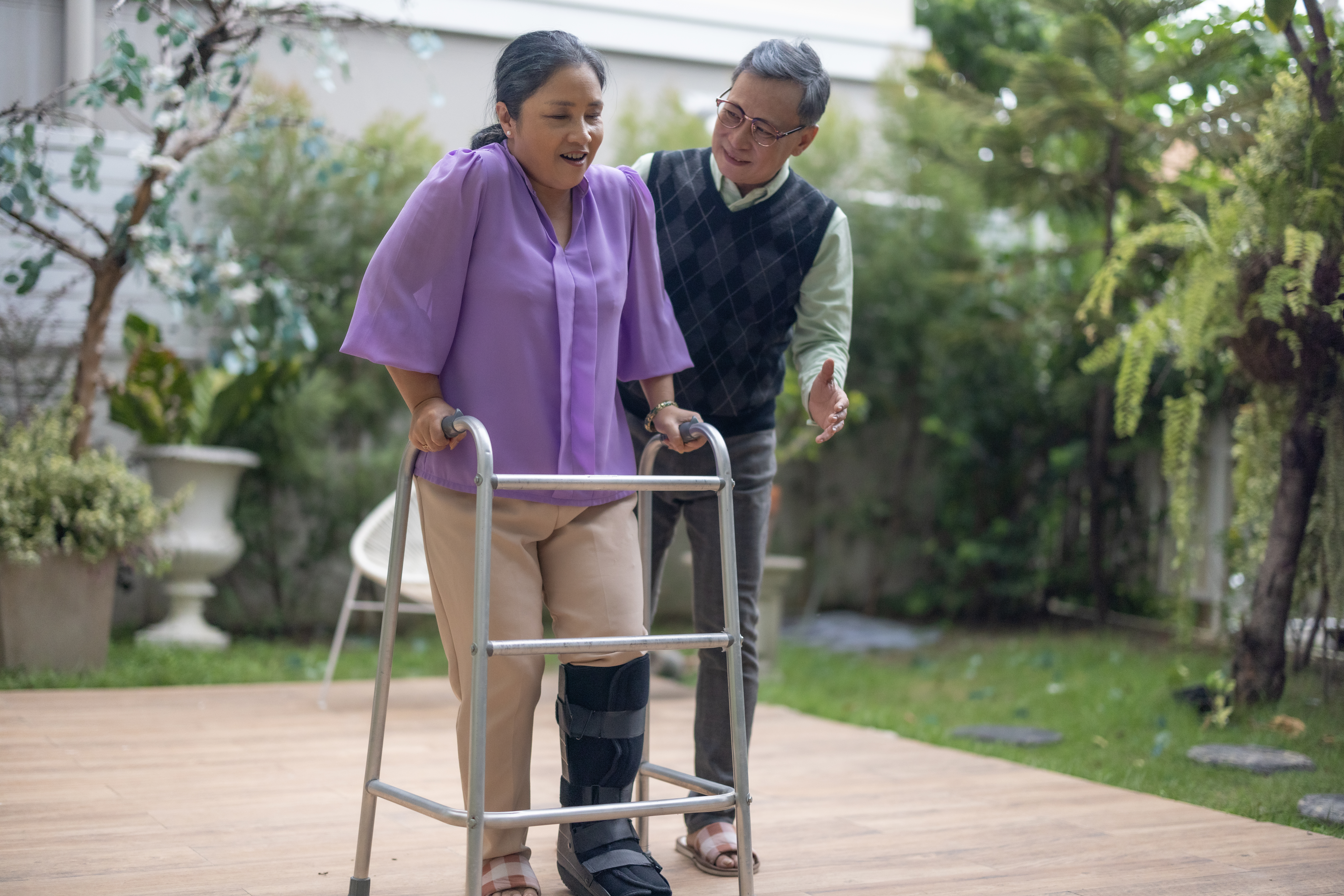 A smiling person assists someone who is using a walking frame