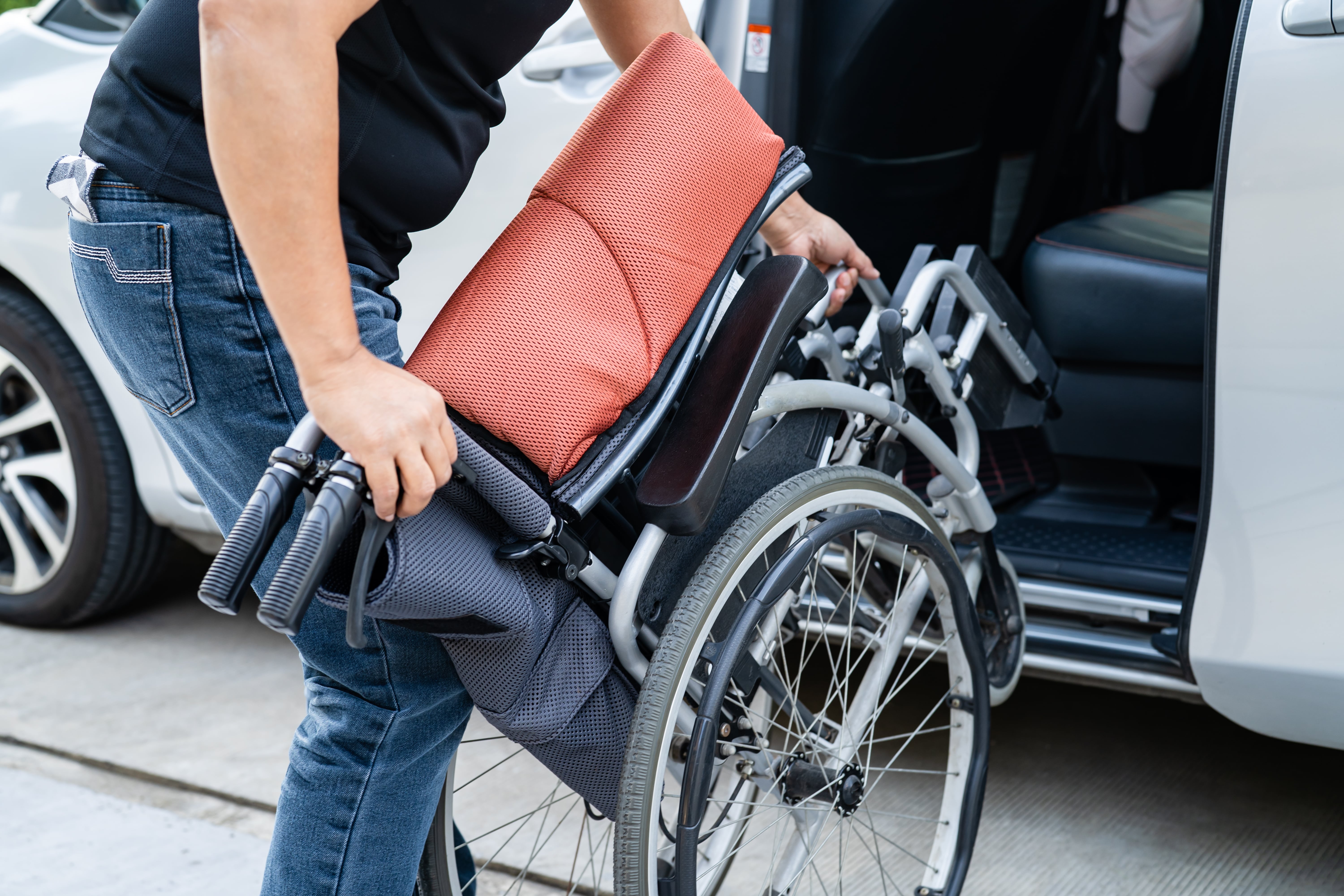 Man lifting a folded wheelchair into a vehicle